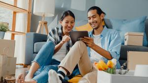 A couple sits on the ground in their new home and shop online on their tablet.