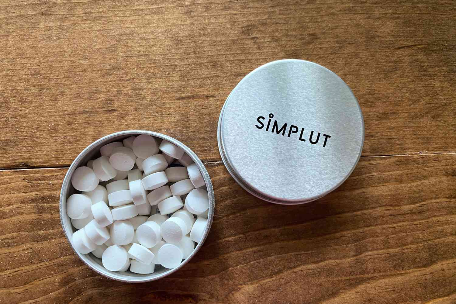 A jar of Simplut Chewable Toothpaste Tablets with Fluoride open on a wooden background