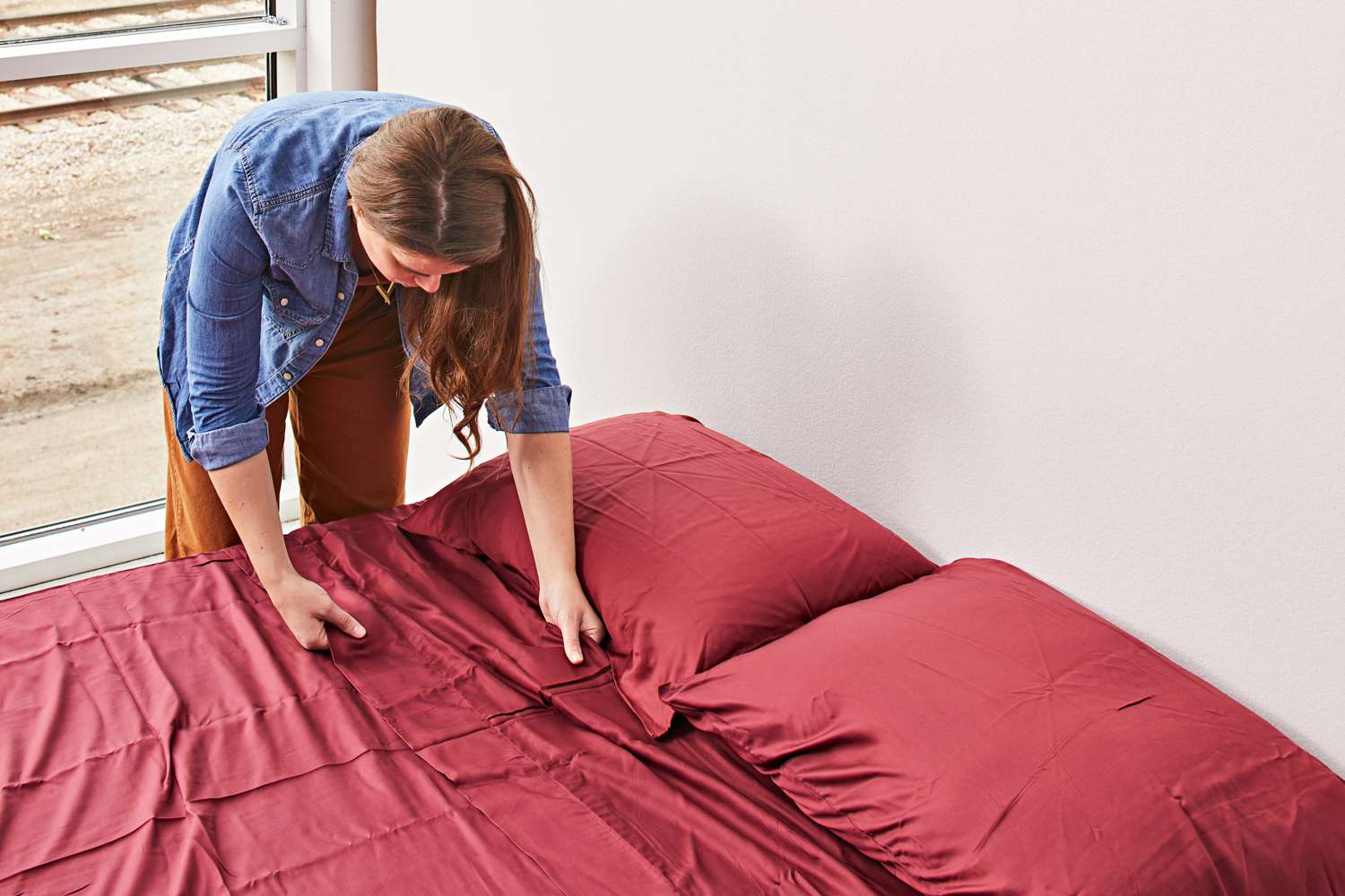 A woman making the bed with California Design Den Bamboo Sheet Set