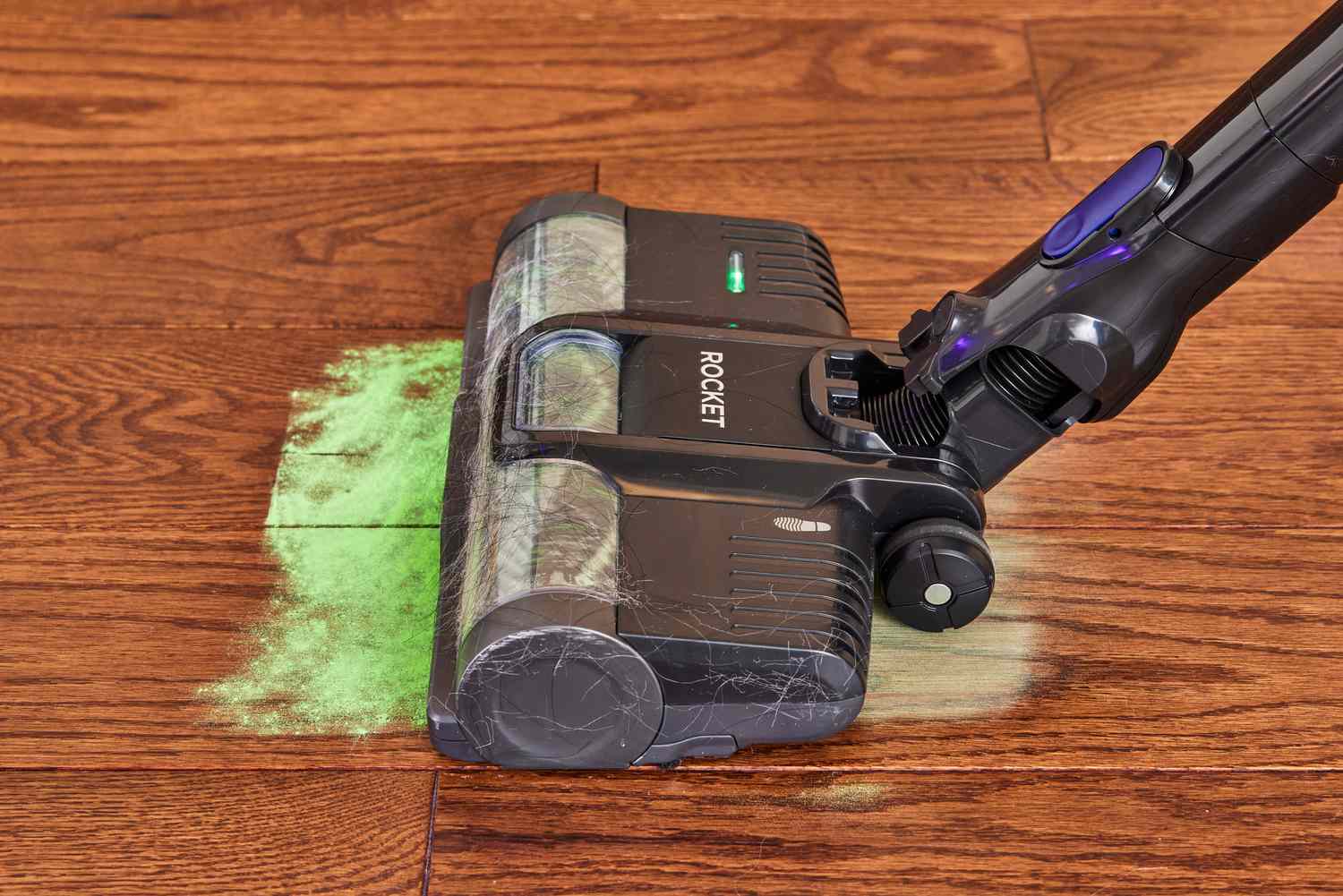 A Shark Pet Cordless Stick Vacuum with XL Dust Cup cleaning a wooden floor filled with green powder