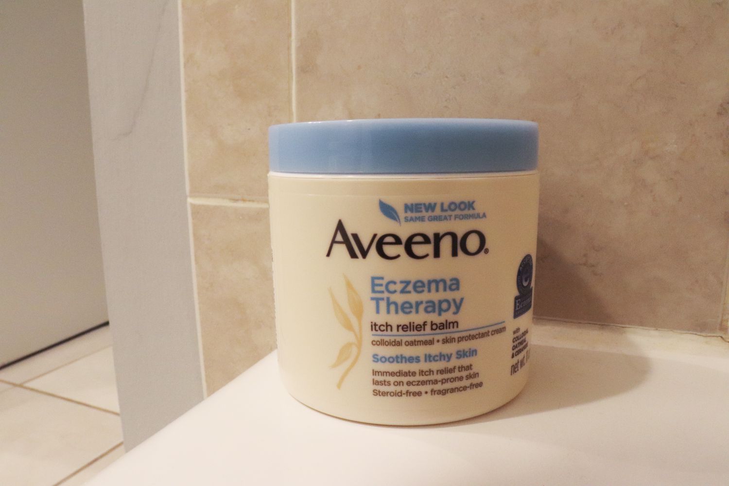 Aveeno Eczema Therapy Nighttime Itch Relief Balm displayed on the edge of a bathroom counter
