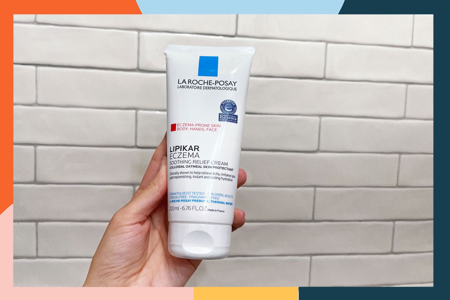 Hand holding La Roche-Posay Lipikar Soothing Relief Eczema Cream in front of a white tile wall