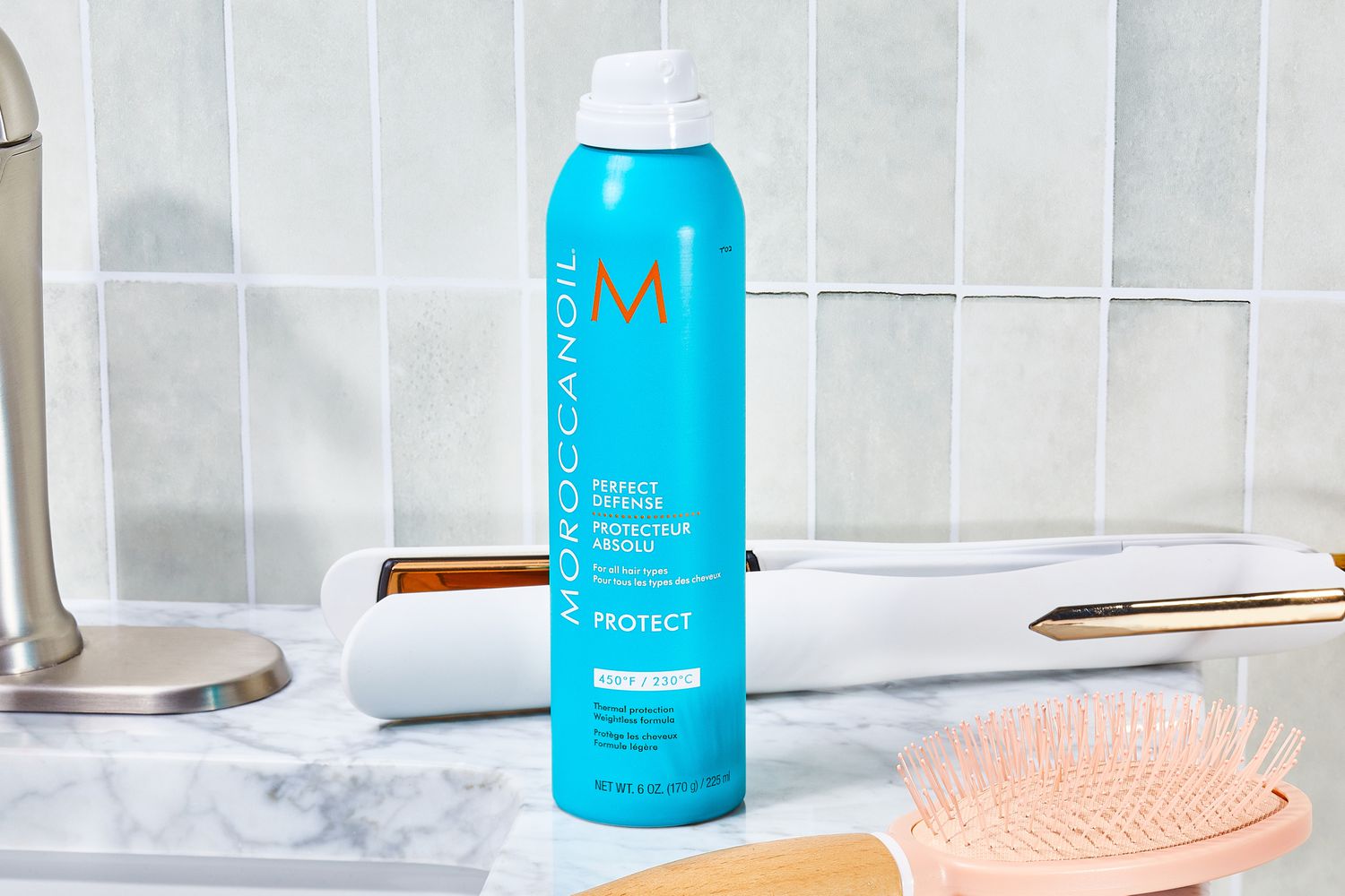Moroccanoil Perfect Defense Heat Protectant bottle sits on bathroom counter with hair styling tools