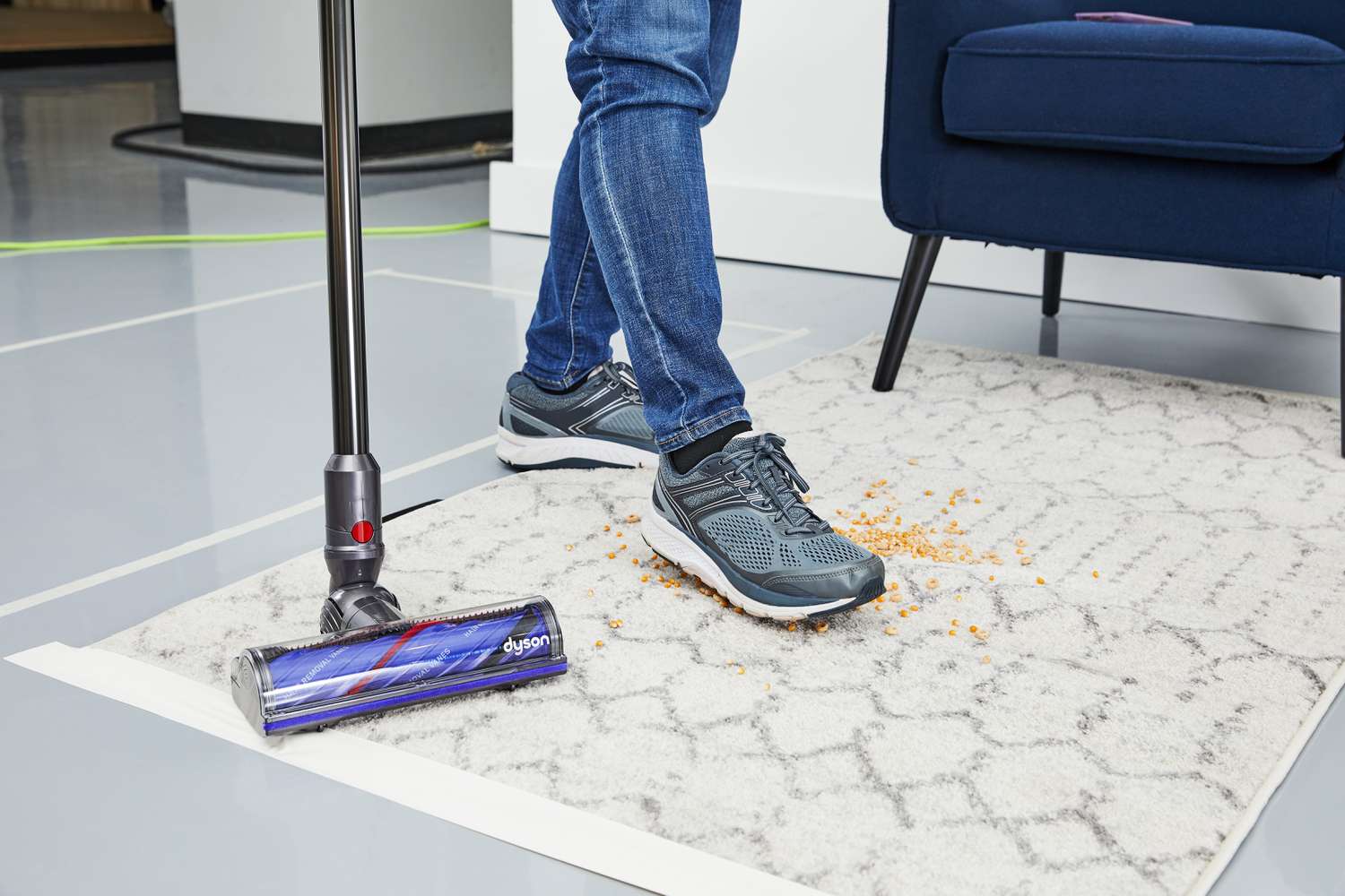 A foot stepping on crumbs on a rug with the Dyson V12 Detect Slim beside it