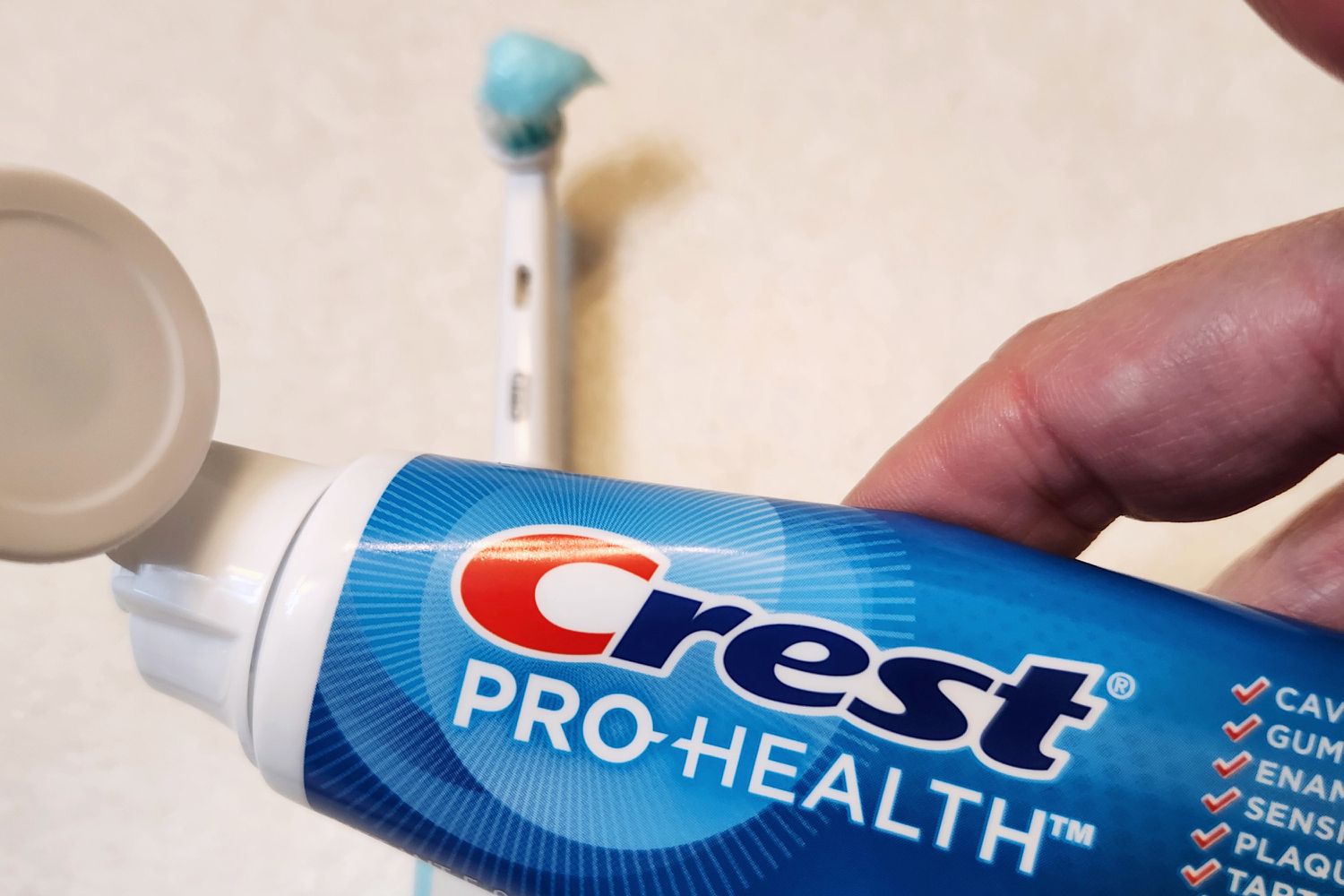 A hand holding a Crest Pro-Health Clean Mint Toothpaste tube over a counter 