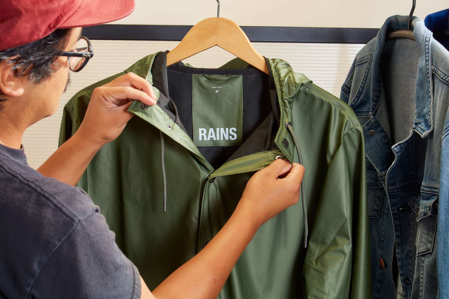 Person opening a Rains Men's Long Jacket on a hanger