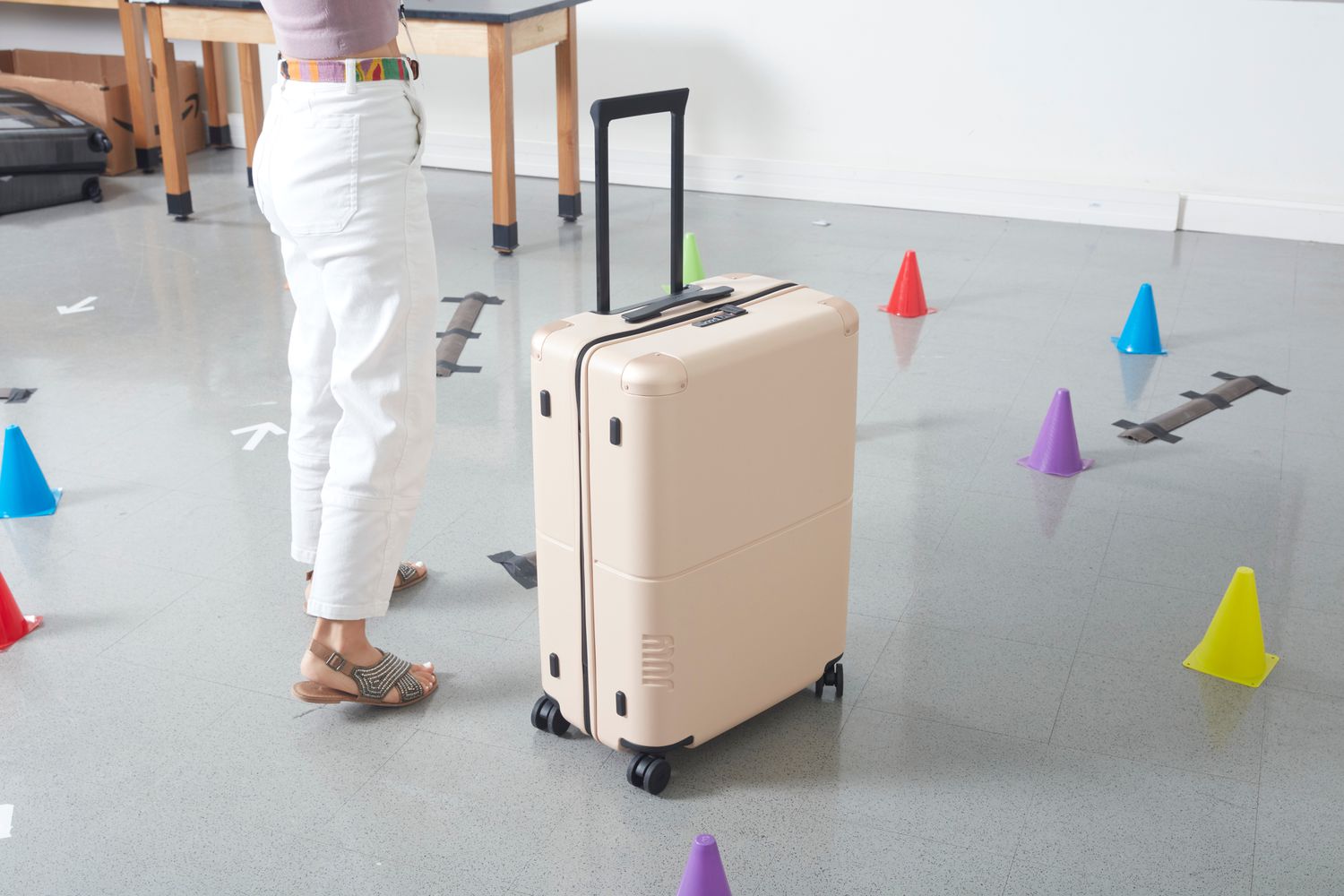 Person standing next to the July Checked Suitcase next to colorful cones during product testing