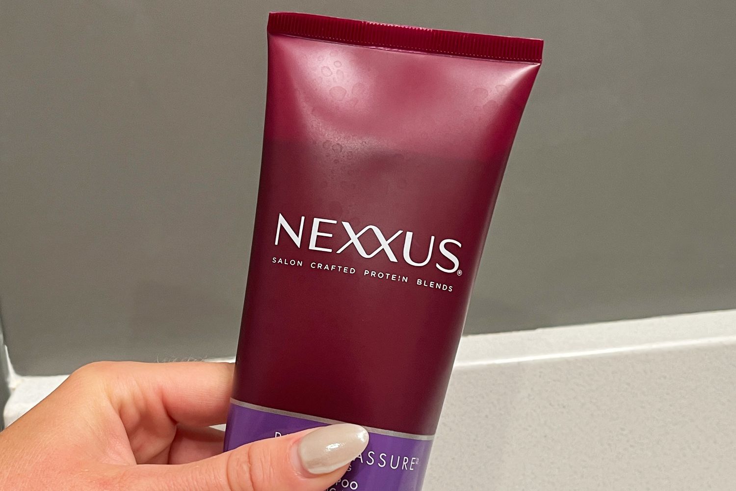 Hand holding a tube of Nexxus Blonde Assure Color Toning Shampoo
