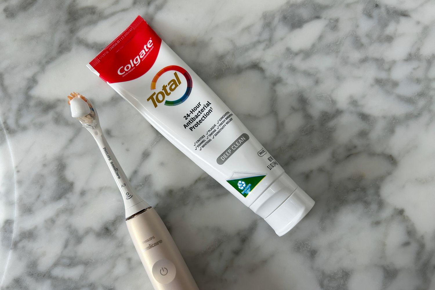 A Colgate Total Deep Clean Toothpaste tube next to a tooth brush loaded with a dot of the toothpaste