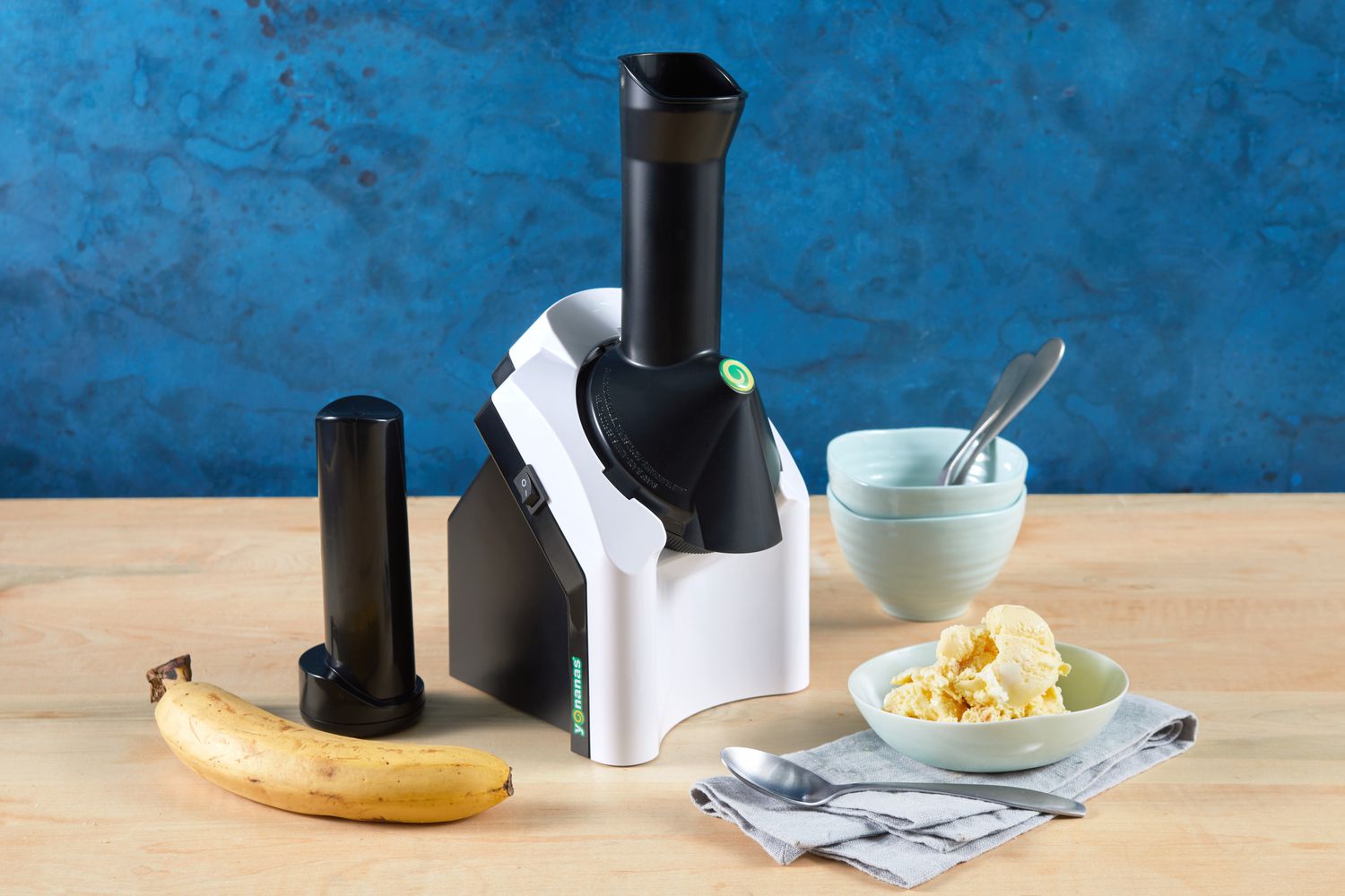 The Yonanas Classic Soft Serve Maker on a wood counter with it's accessories and finished ice cream.