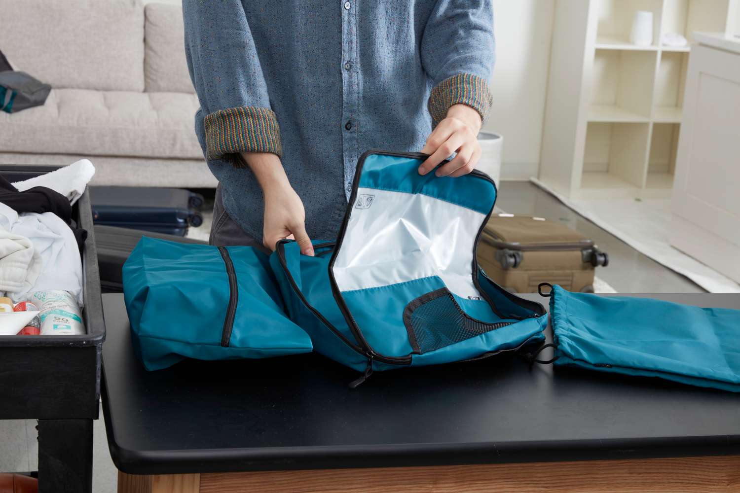 Person unzipping a Veken Packing Cube beside laundry and shoe bag on a black tabletop