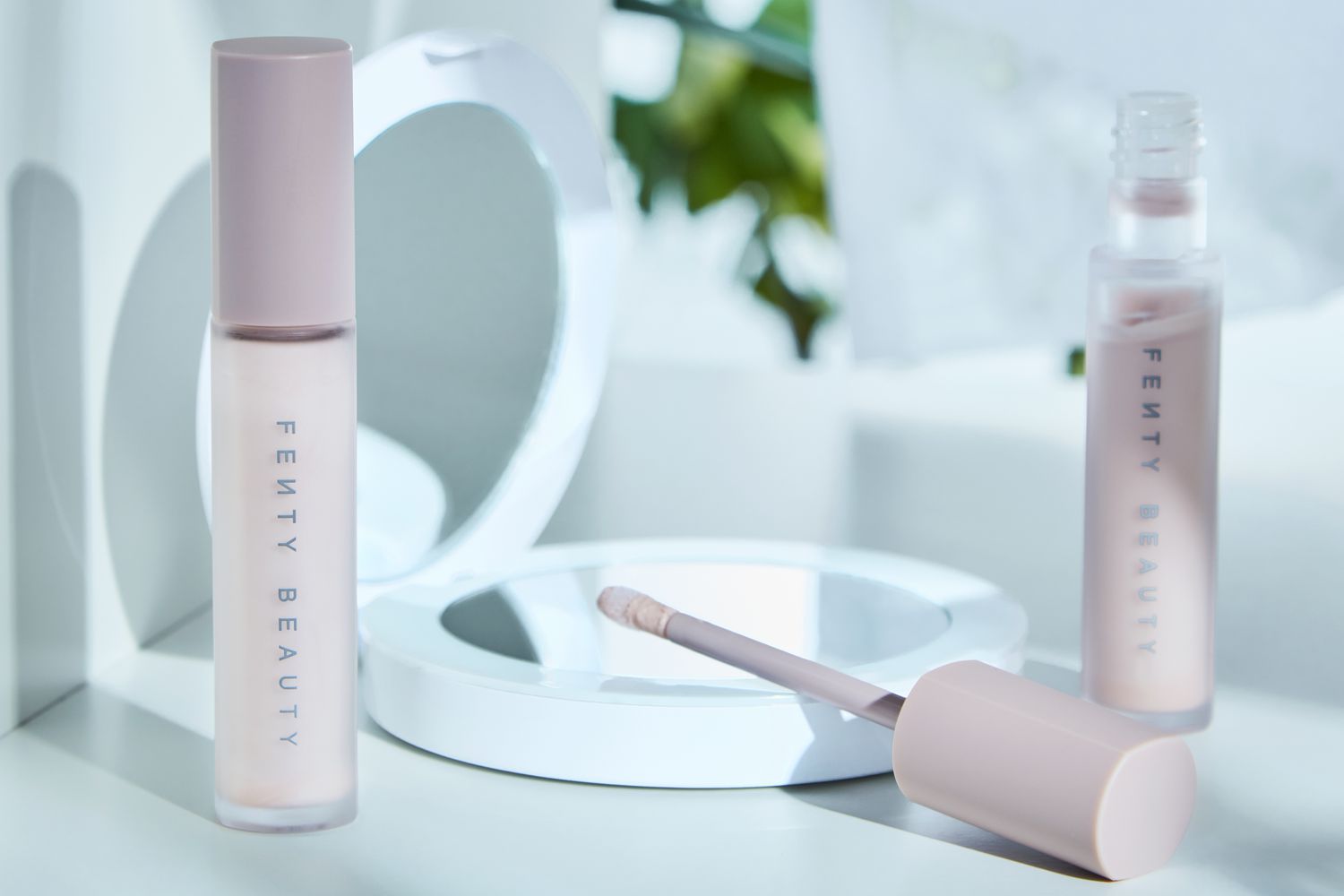Two bottles of Fenty Beauty Pro Filt'r Amplifying Eye Primer displayed on a white surface next to a compact mirror