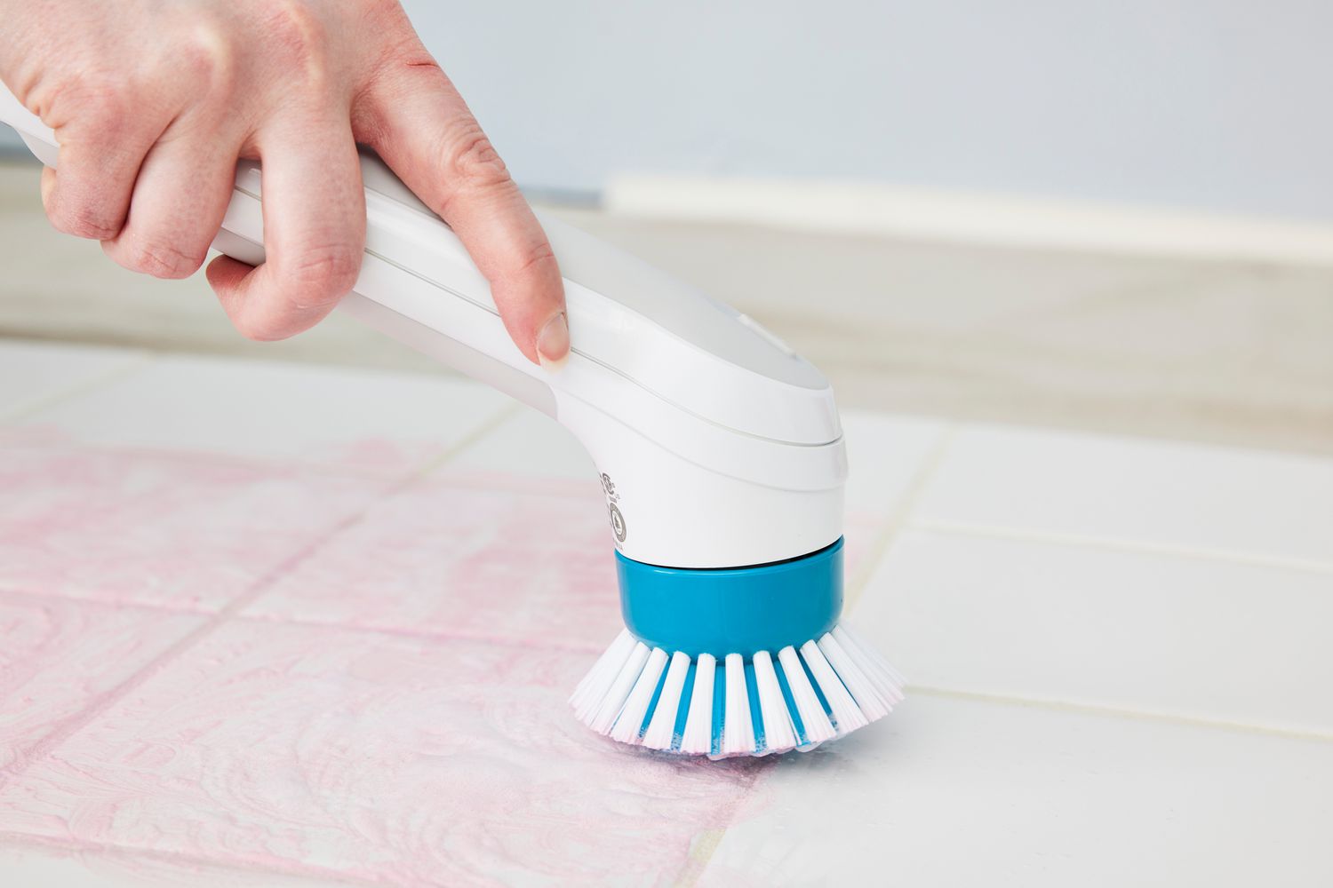 A hand scrubs tile with a Black+Decker Grimebuster Pro Power Scrubber Brush