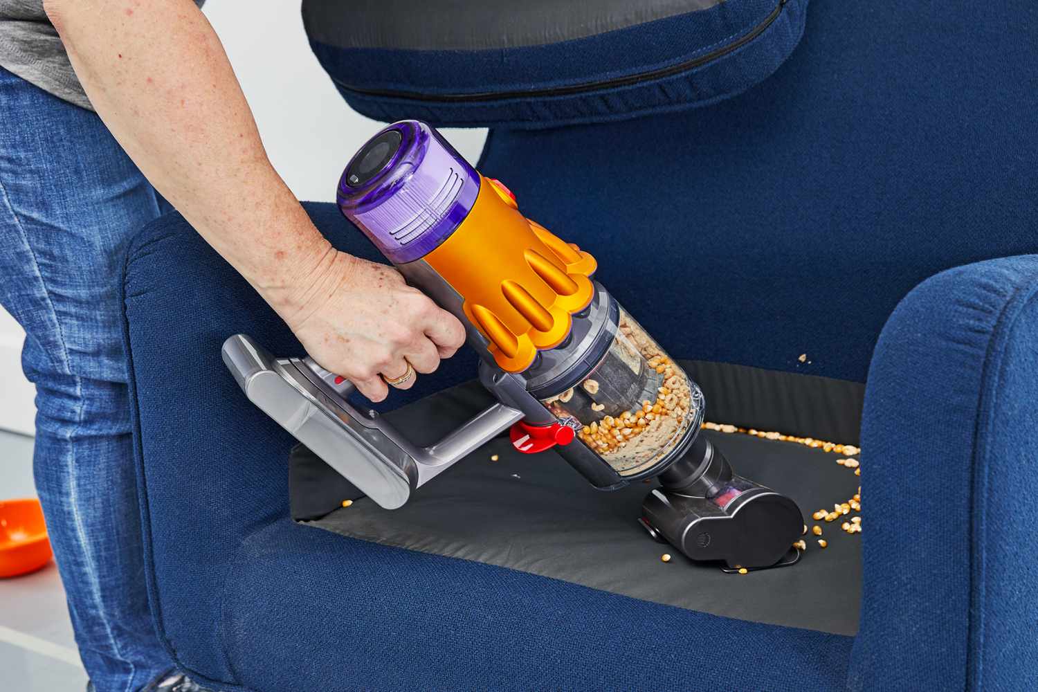 A hand pushing the Dyson V12 Detect Slim over popcorn kettle inside a armchair