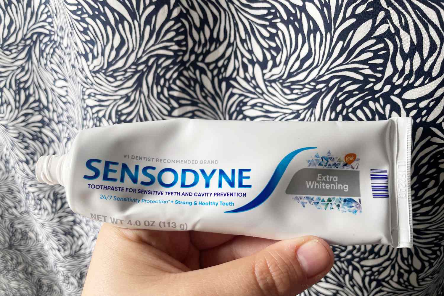 A hand holding a tube of Sensodyne Extra Whitening Toothpaste