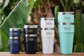 Four Yeti reusable tumblers in different colors on a table with plants in the background