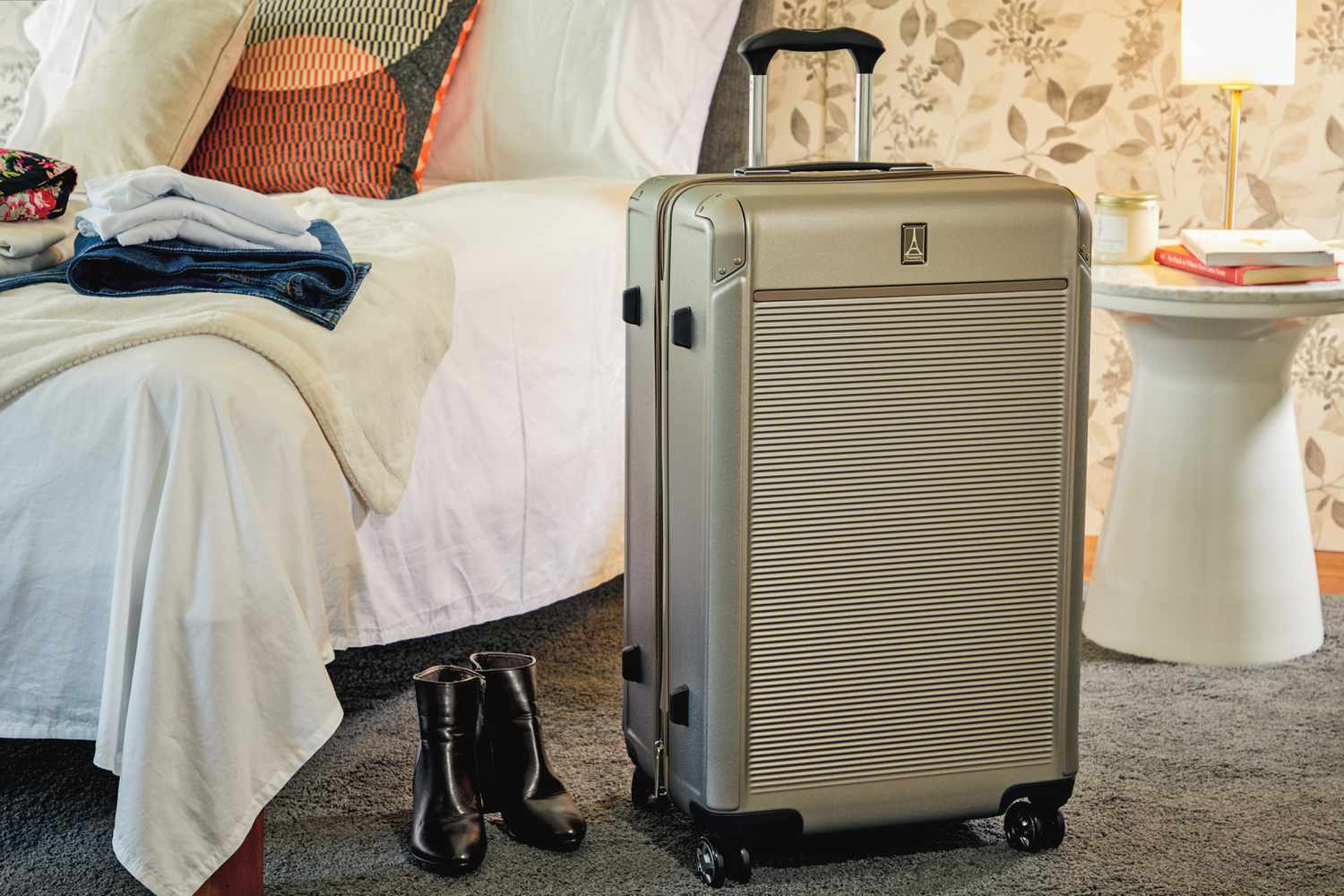 Silver Travelpro Platinum Elite Large Check-In Expandable Hardside Spinner displayed next to a bed and white table