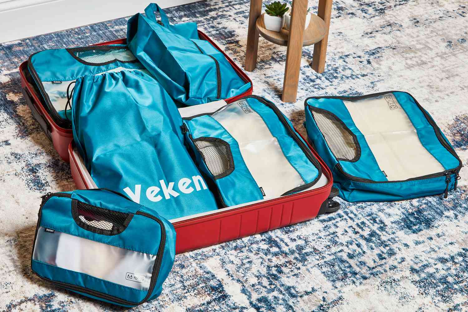 Veken Packing Cubes next to Laundry and Shoe Bag placed in a suitcase on a blue print rug