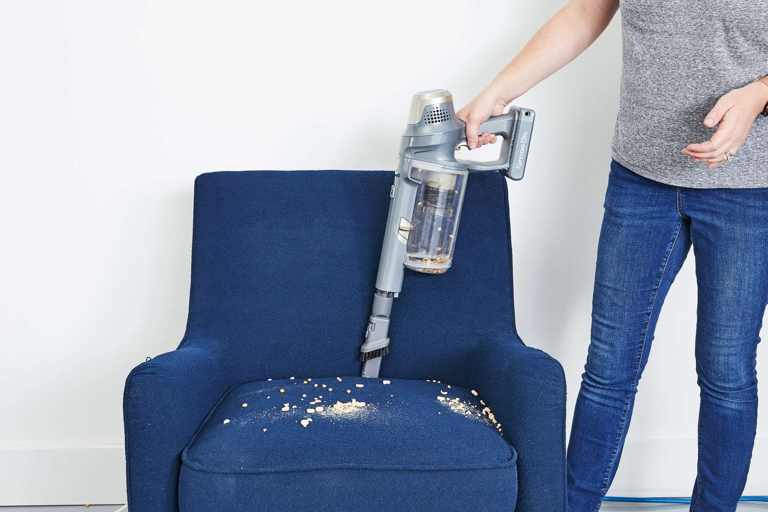 Person using handheld attachment Kenmore DS4095 Elite Cordless Stick Vacuum with EasyReach Wand to clean chair