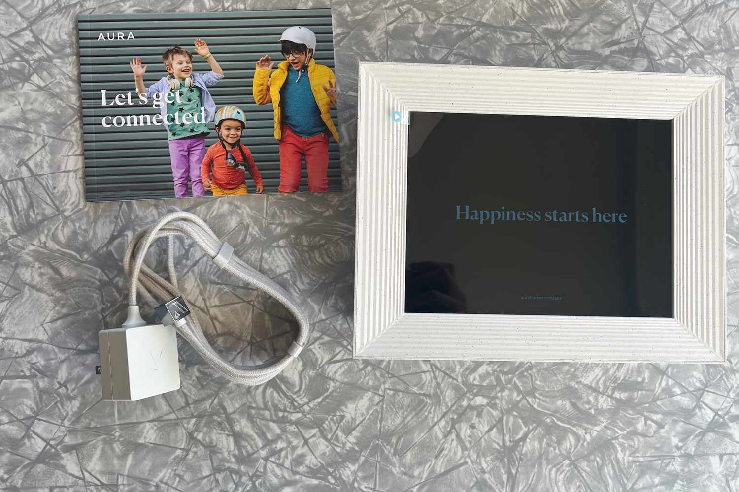 Aura Mason WiFi Digital Picture Frame on a gray counter with its welcome card and charger