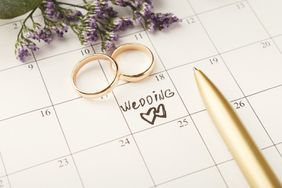 Word wedding, two hearts and gold rings on calendar with sweet purple flowers