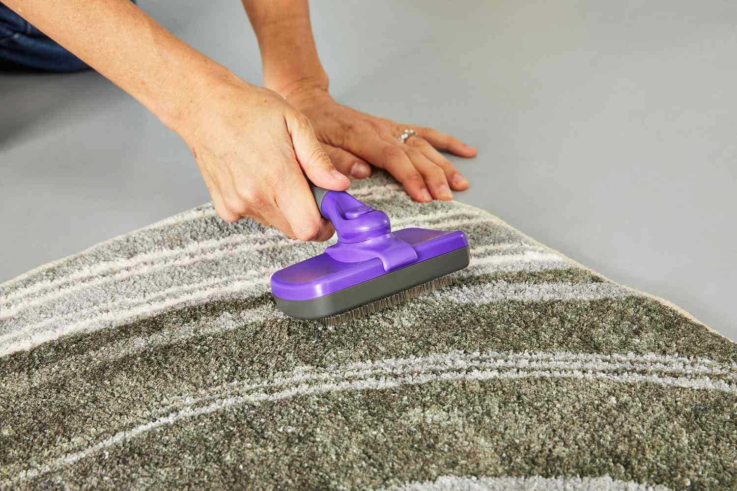 A person brushing the West Elm Waterfall Washable Rug