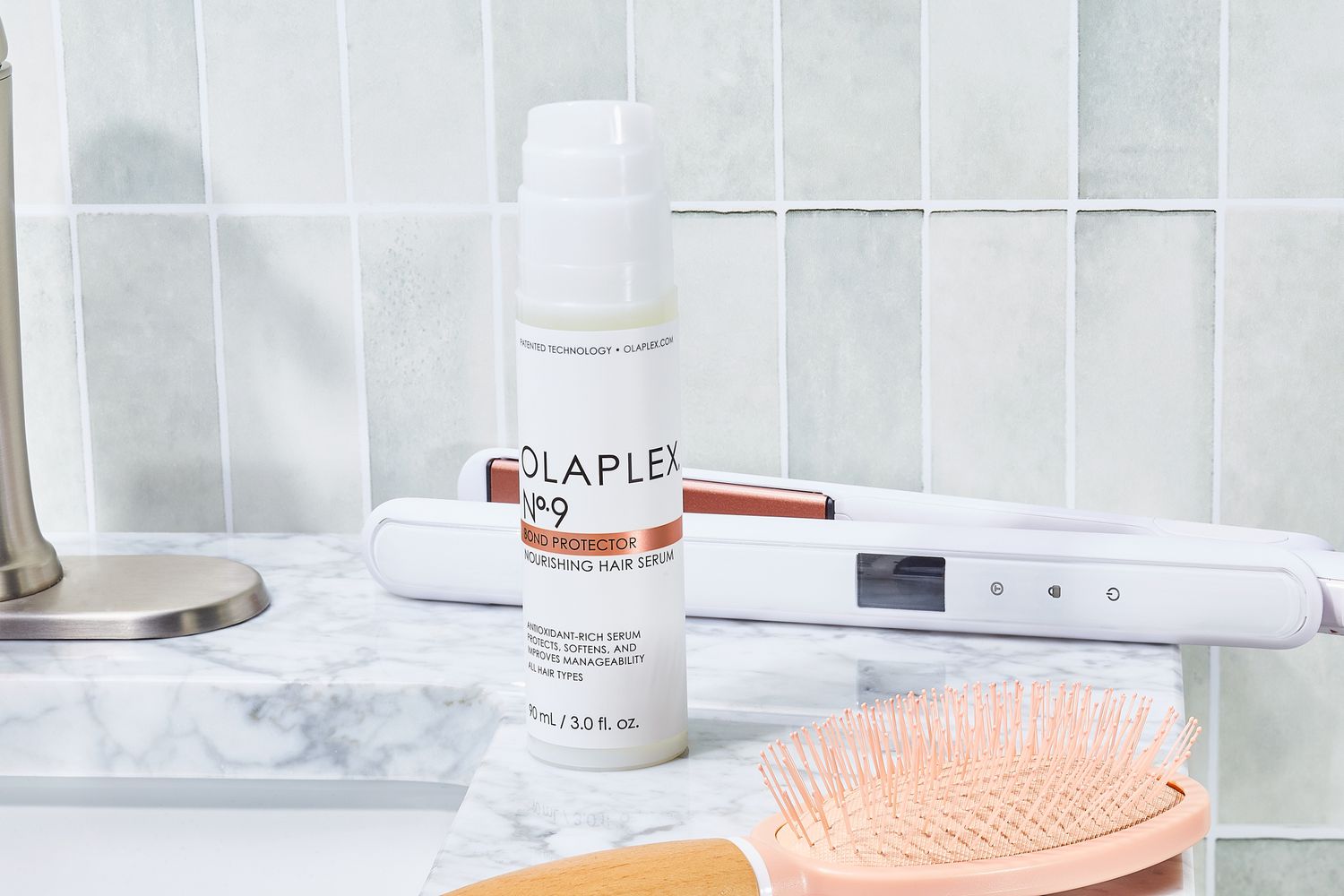Olaplex No. 9 Bond Protector Nourishing Hair Serum bottle sits on bathroom counter with hair styling tools