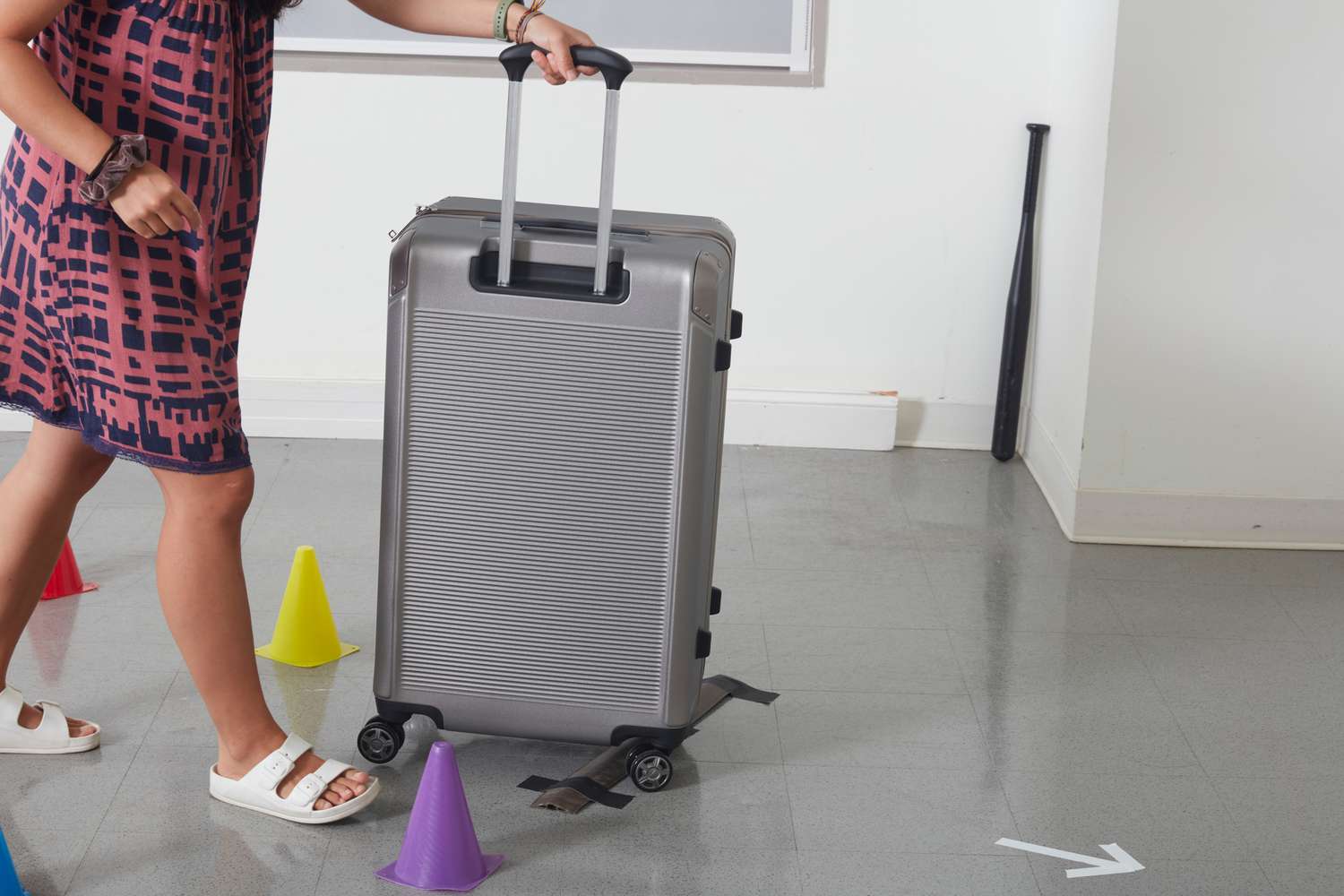 Woman rolling gray Travelpro Platinum Elite Large Check-In Expandable Hardside Spinner between colorful cones