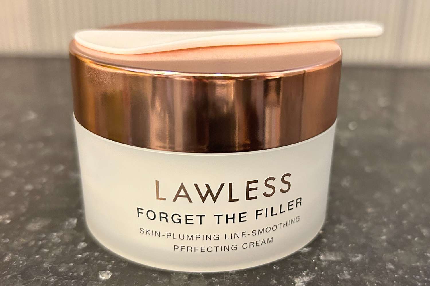 A jar of Lawless Forget the Filler Skin-Plumping Line-Smoothing Perfecting Cream with an applicator spoon