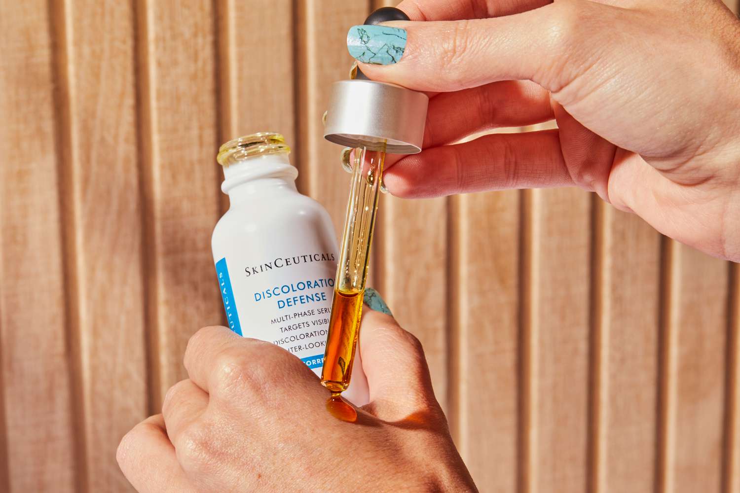 hand dispensing Skinceuticals Discoloration Defense from dropper onto back of other hand