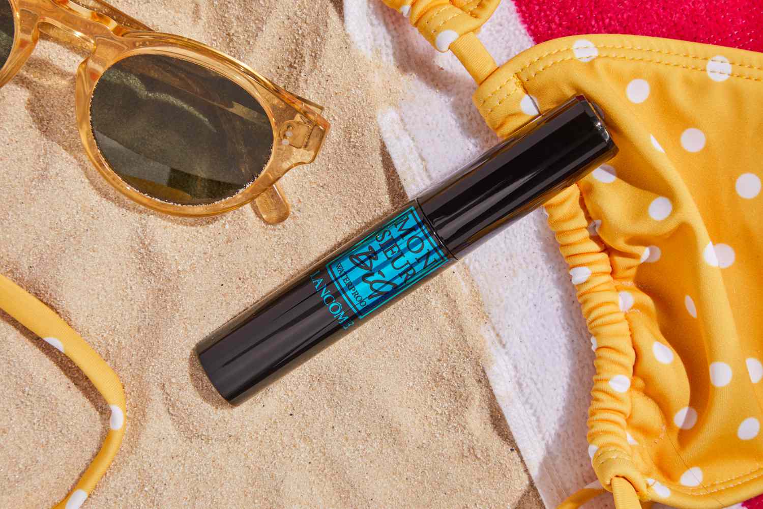 Lancôme Monsieur Big Volumizing Waterproof Mascara on sand next to sunglasses and swimwear