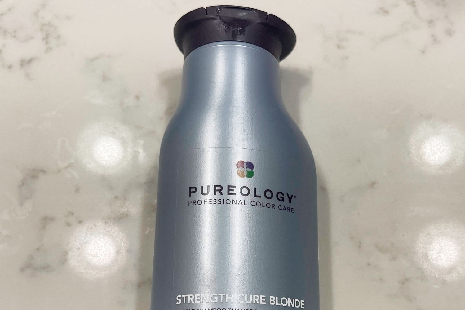 A bottle of Pureology Strength Cure Blonde Shampoo on a marble surface 