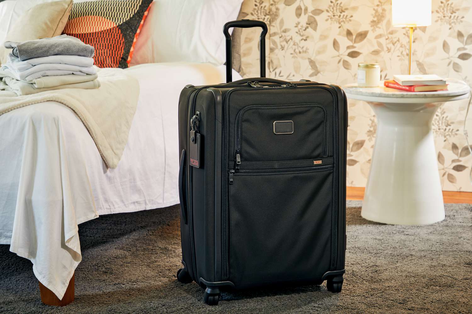 Tumi Alpha 3 Short Trip Expandable Packing Case displayed in front of a bed and a white bedside table