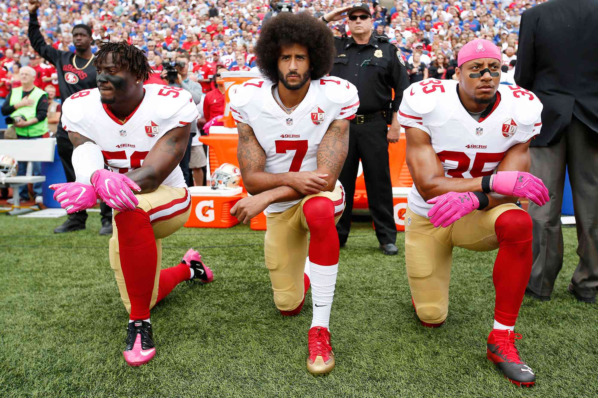 Eli Harold #58, Colin Kaepernick #7 and Eric Reid #35 of the San Francisco 49ers kneel in protest on the sideline, during the anthem