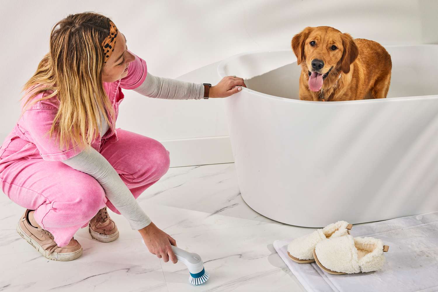 Woman scrubs a marble floor with a Black+Decker Grimebuster Pro Power Scrubber Brush next to a tub with a golden retriever inside