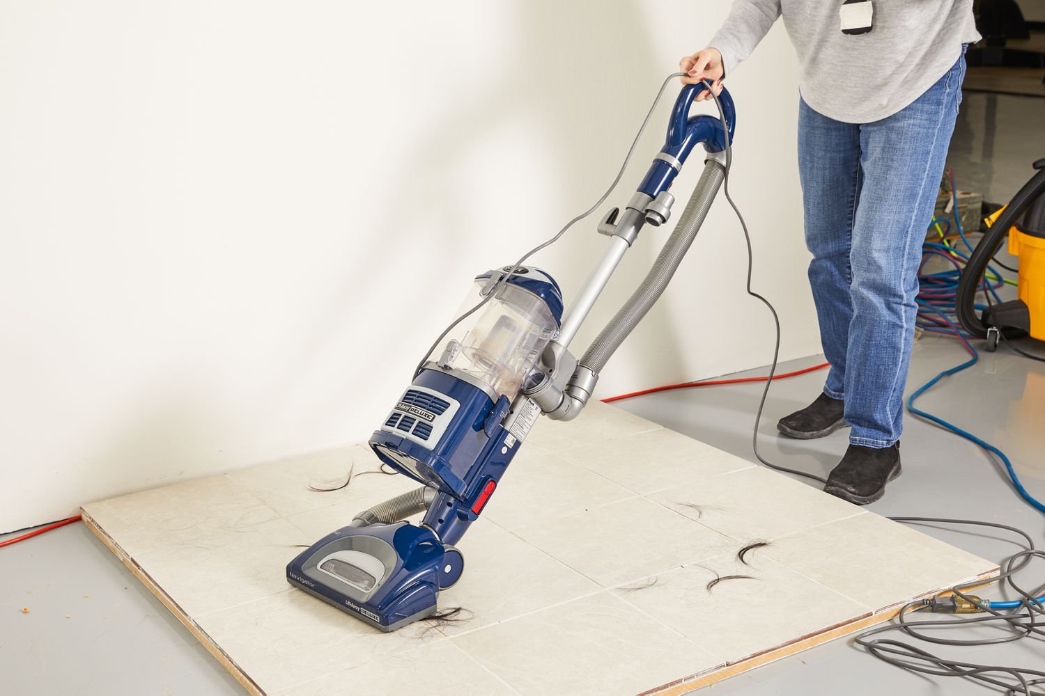 Person using the Shark NV360 Navigator Lift-Away Deluxe Upright Vacuum to clean hair from tile floor