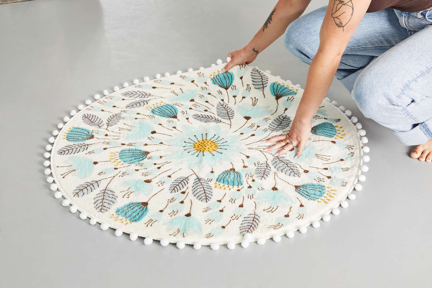 A person adjusting the Uphome Pom Pom Round Floral Rug on the floor