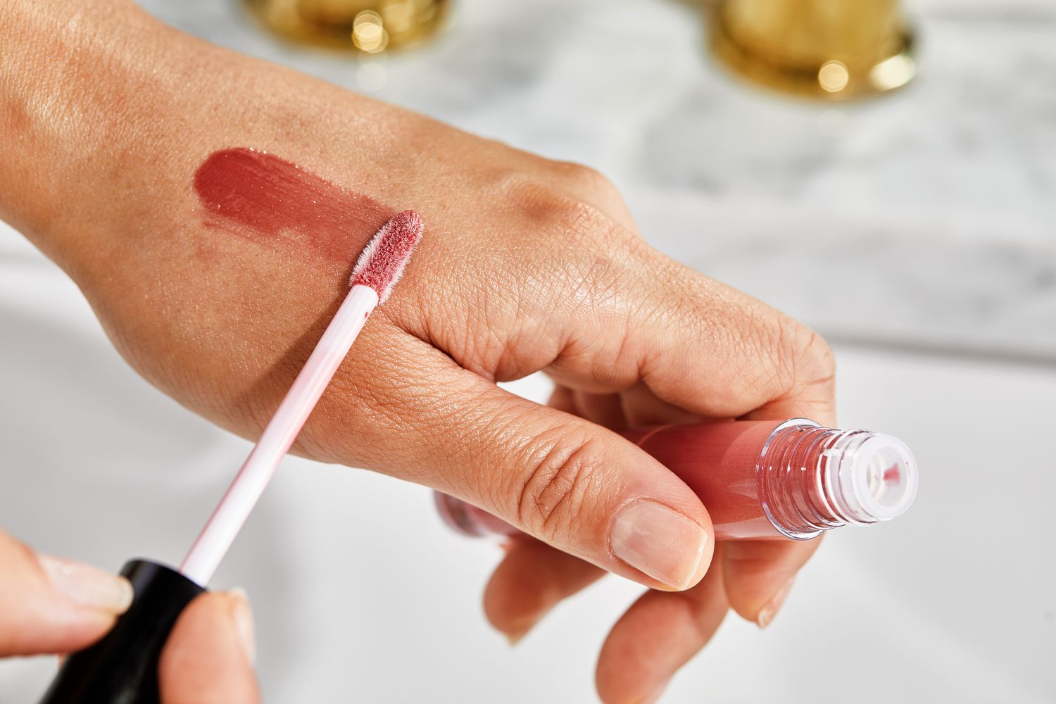 Close up of a person applying Pat McGrath LUST Gloss to the back of their hand