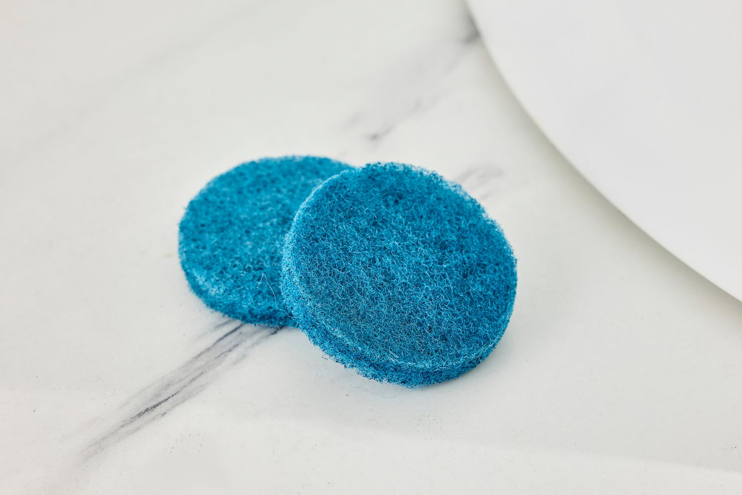 Two blue scrub pads lying on a marble counter