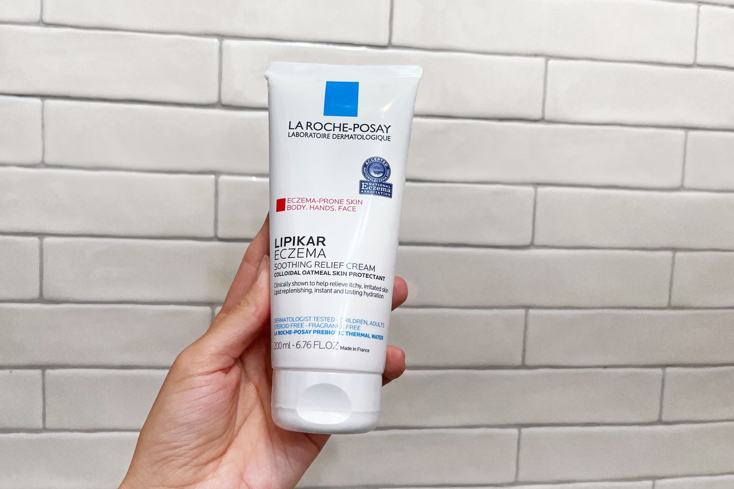Person holding a tube of La Roche-Posay Lipikar Eczema Soothing Relief Cream in front of a tile wall