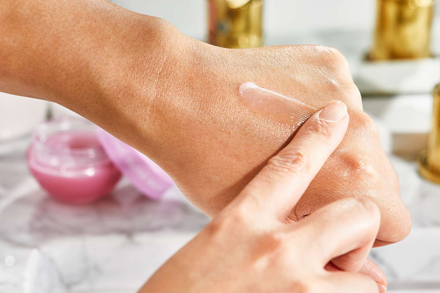 Close up of a person applying Glow Recipe Plum Plump Hyaluronic Acid Lip Gloss Balm to the back of their hand