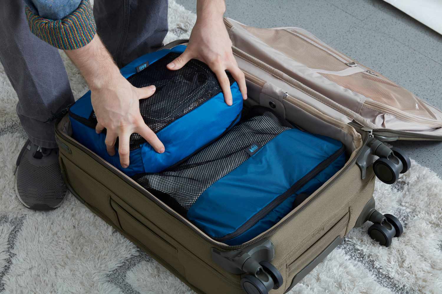 Person packing a REI Co-op Expandable Packing Cube Set into a suitcase on rug