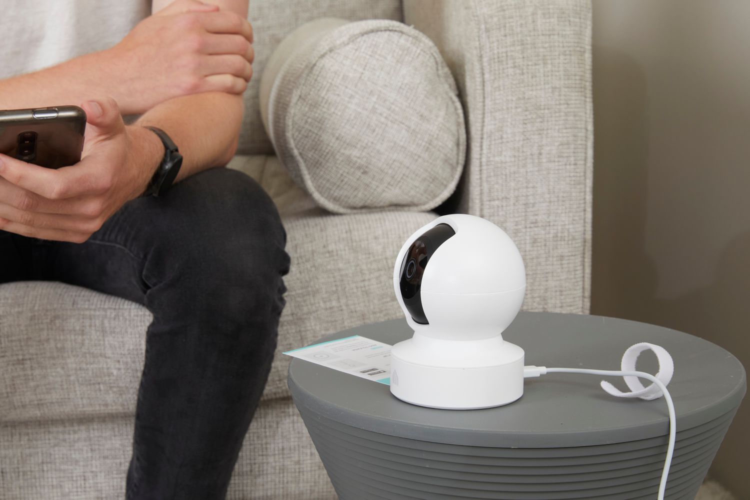 Person looking at their phone on a couch next to the Kasa Indoor Pan/Tilt Smart Security Camera