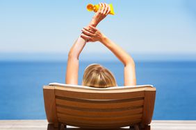 Woman applying sunscreen while relaxing in a lounge chair in front of the ocean