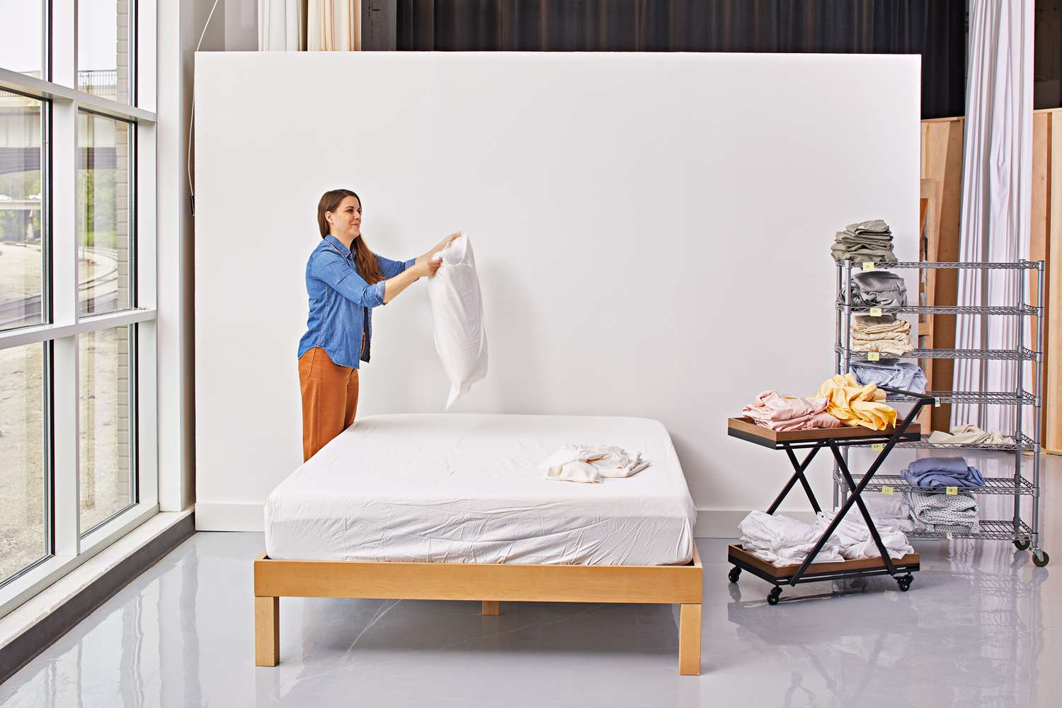 Woman adding white set of The Company Store Company Cotton Rayon Made From Bamboo Sateen Sheet Set to a bed and pillow