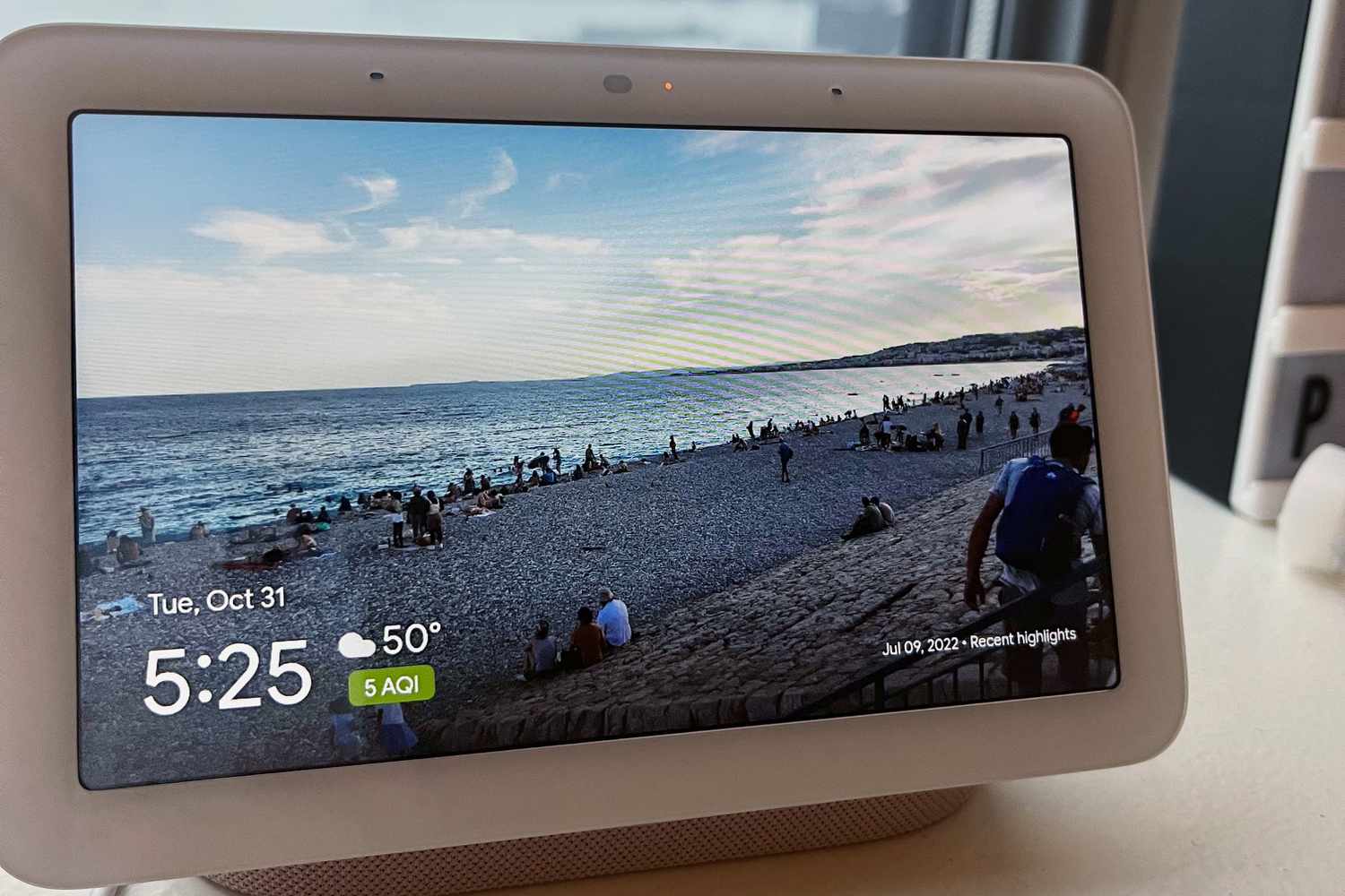 The Google Nest Hub 2nd Gen sitting on a window sill with a picture of a beach displayed.
