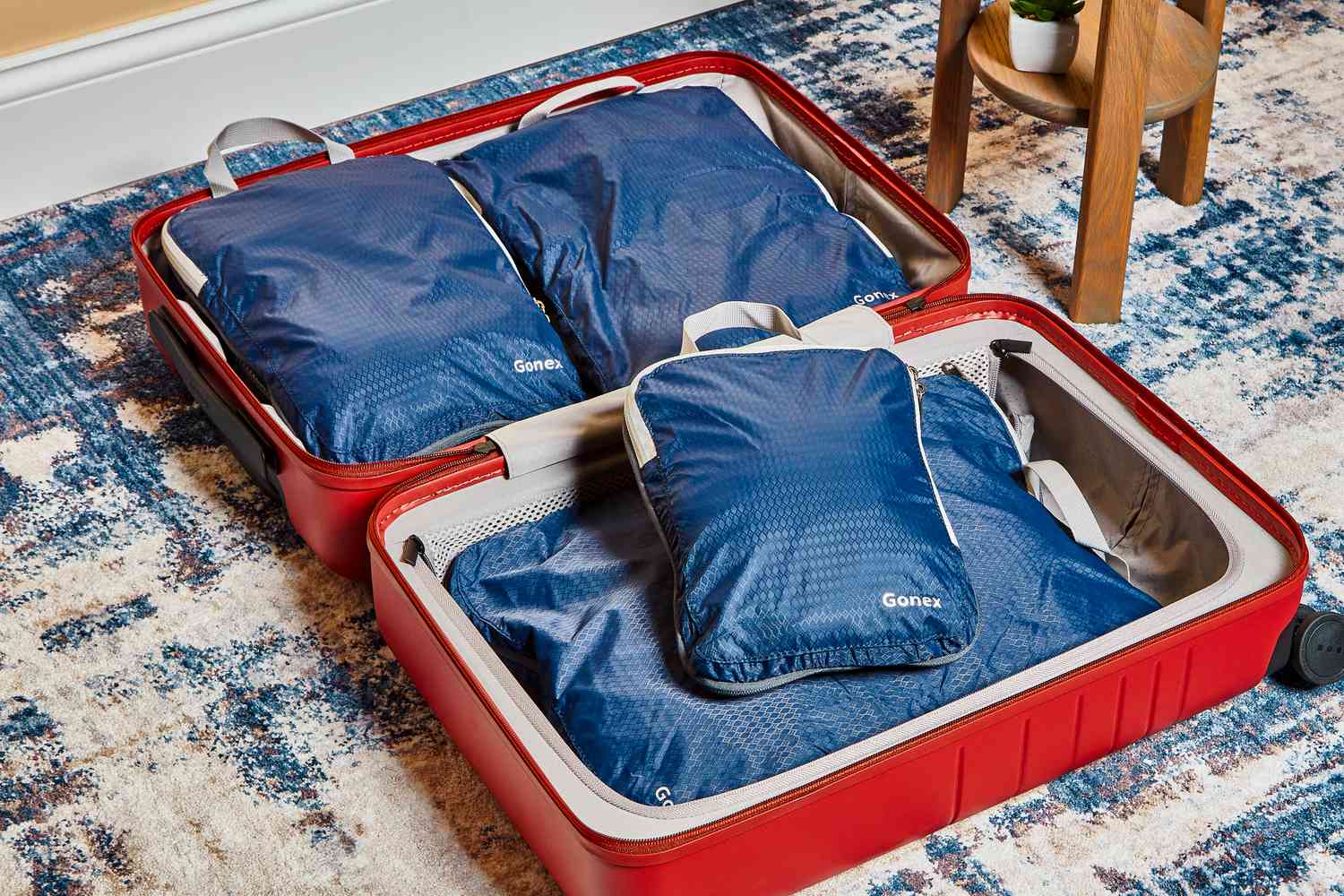 Set of blue Gonex Compression Packing Cubes packed in a red suitcase on a blue print rug
