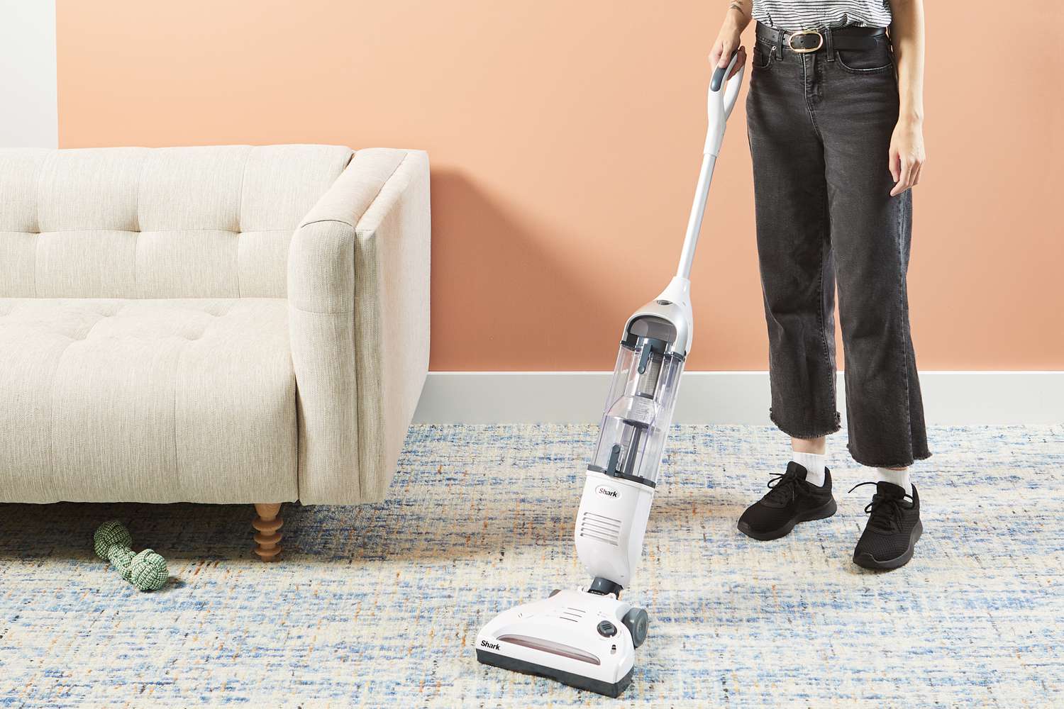 A person using the Shark SV1106 Navigator Freestyle Upright Bagless Cordless Stick Vacuum on a rug in a living room