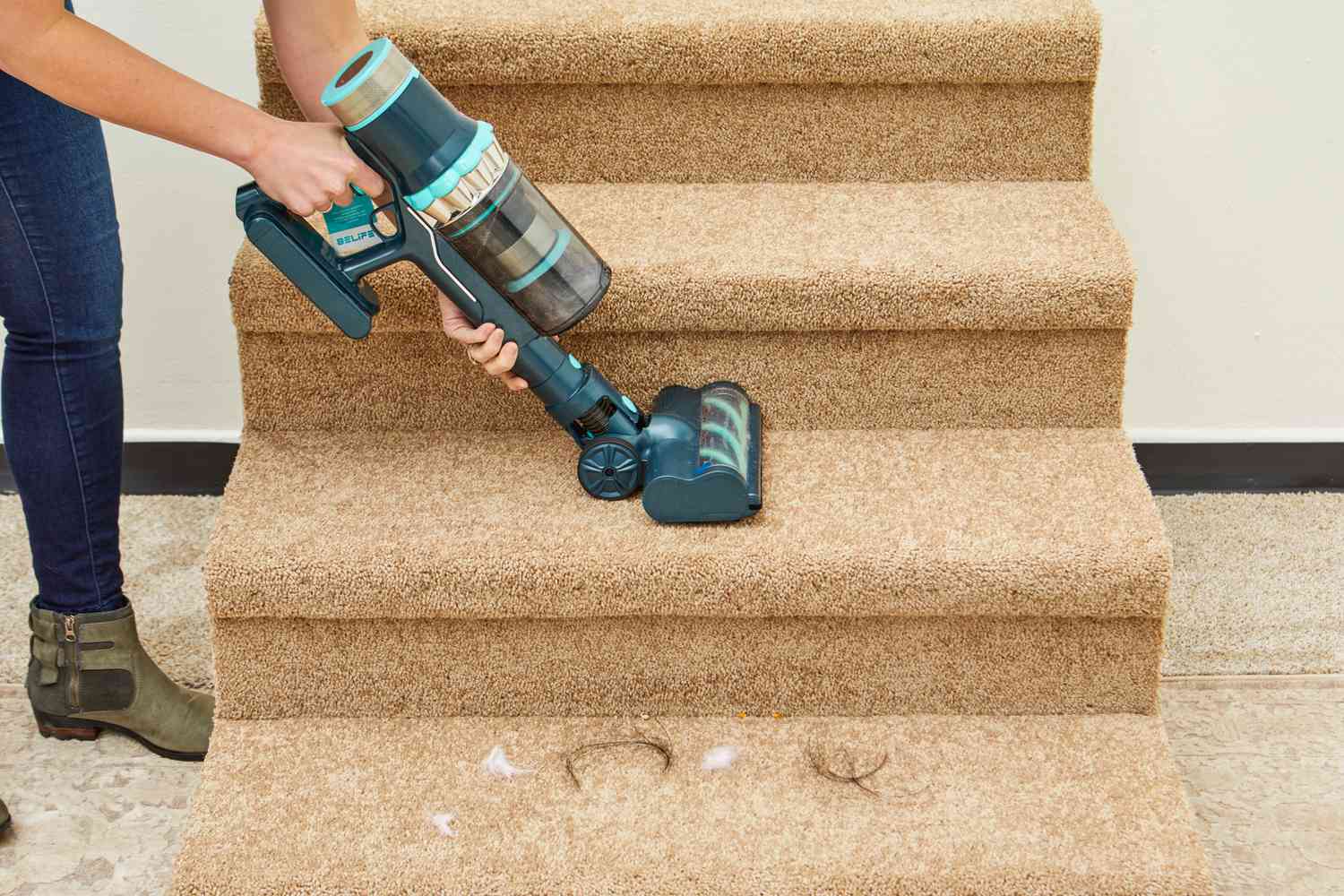 A person uses the Belife V12 Cordless Vacuum Cleaner's handheld attachment on carpeted stairs.