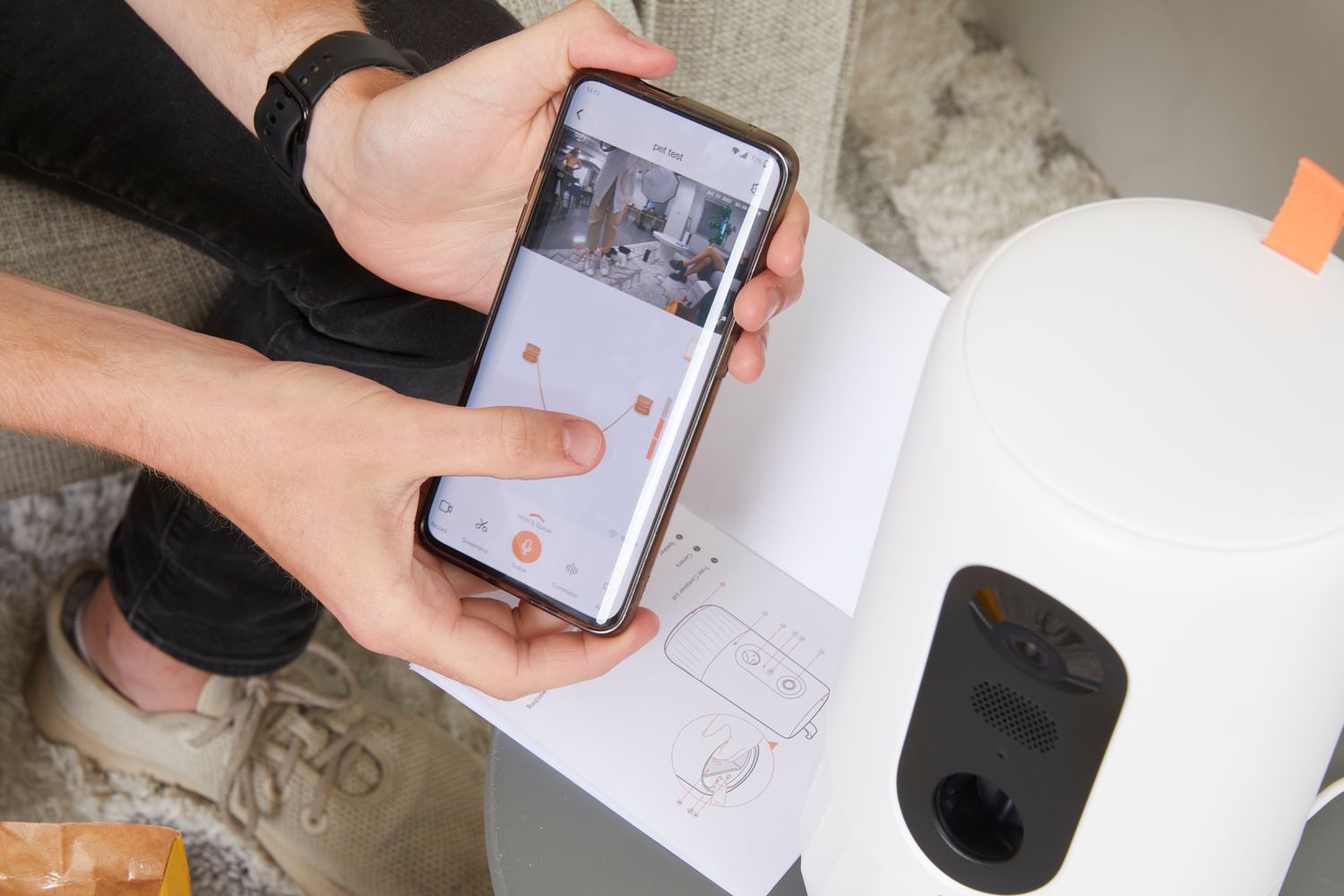 Person holding up phone next to the Eufy Pet Dog Camera D605 to display the app